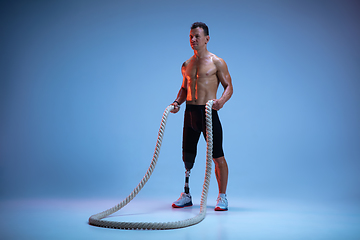 Image showing Athlete with disabilities or amputee isolated on blue studio background. Professional male sportsman with leg prosthesis training with weights in neon