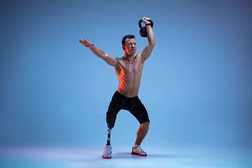 Image showing Athlete with disabilities or amputee isolated on blue studio background. Professional male sportsman with leg prosthesis training with weights in neon