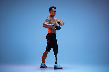 Image showing Athlete with disabilities or amputee isolated on blue studio background. Professional male sportsman with leg prosthesis training with weights in neon