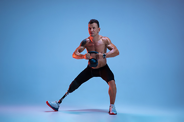 Image showing Athlete with disabilities or amputee isolated on blue studio background. Professional male sportsman with leg prosthesis training with weights in neon