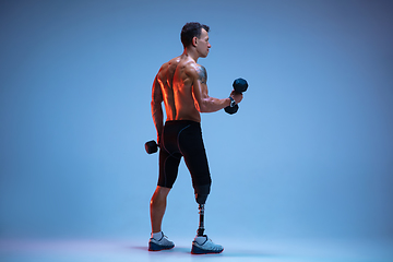 Image showing Athlete with disabilities or amputee isolated on blue studio background. Professional male sportsman with leg prosthesis training with weights in neon