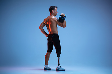 Image showing Athlete with disabilities or amputee isolated on blue studio background. Professional male sportsman with leg prosthesis training with weights in neon