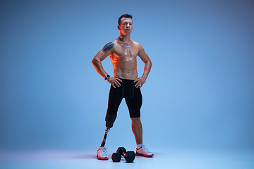 Image showing Athlete with disabilities or amputee isolated on blue studio background. Professional male sportsman with leg prosthesis training with weights in neon