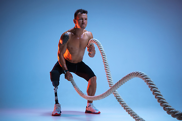 Image showing Athlete with disabilities or amputee isolated on blue studio background. Professional male sportsman with leg prosthesis training with weights in neon