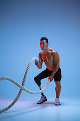 Image showing Athlete with disabilities or amputee isolated on blue studio background. Professional male sportsman with leg prosthesis training with weights in neon