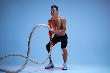 Image showing Athlete with disabilities or amputee isolated on blue studio background. Professional male sportsman with leg prosthesis training with weights in neon