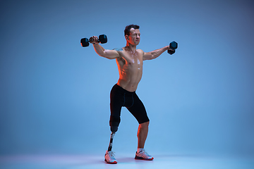 Image showing Athlete with disabilities or amputee isolated on blue studio background. Professional male sportsman with leg prosthesis training with weights in neon
