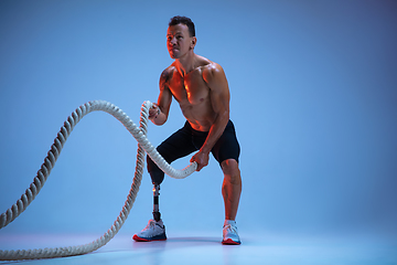 Image showing Athlete with disabilities or amputee isolated on blue studio background. Professional male sportsman with leg prosthesis training with weights in neon