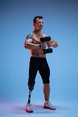 Image showing Athlete with disabilities or amputee isolated on blue studio background. Professional male sportsman with leg prosthesis training with weights in neon