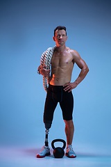 Image showing Athlete with disabilities or amputee isolated on blue studio background. Professional male sportsman with leg prosthesis training with weights in neon