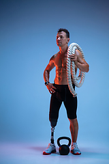 Image showing Athlete with disabilities or amputee isolated on blue studio background. Professional male sportsman with leg prosthesis training with weights in neon