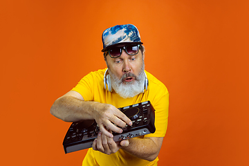 Image showing Senior hipster man using devices, gadgets on orange background. Tech and joyful elderly lifestyle concept