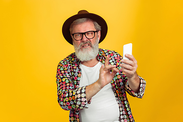 Image showing Senior hipster man wearing eyeglasses posing on yellow background. Tech and joyful elderly lifestyle concept