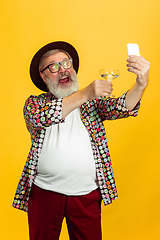 Image showing Senior hipster man wearing eyeglasses posing on yellow background. Tech and joyful elderly lifestyle concept