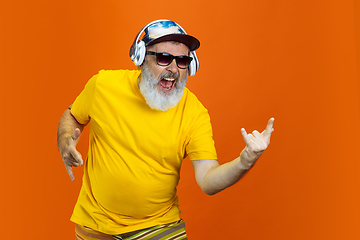 Image showing Senior hipster man using devices, gadgets on orange background. Tech and joyful elderly lifestyle concept