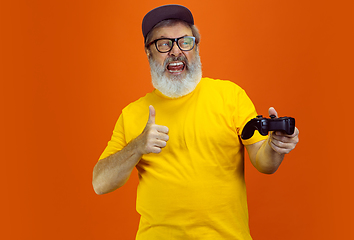 Image showing Senior hipster man using devices, gadgets on orange background. Tech and joyful elderly lifestyle concept