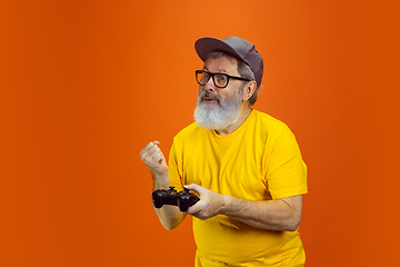 Image showing Senior hipster man using devices, gadgets on orange background. Tech and joyful elderly lifestyle concept