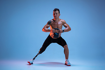 Image showing Athlete with disabilities or amputee isolated on blue studio background. Professional male sportsman with leg prosthesis training with weights in neon