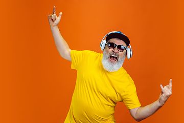 Image showing Senior hipster man using devices, gadgets on orange background. Tech and joyful elderly lifestyle concept