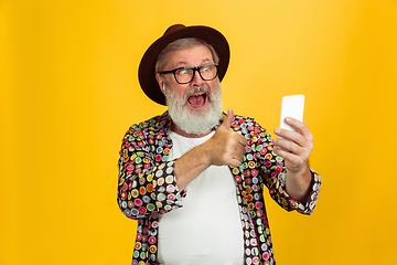 Image showing Senior hipster man wearing eyeglasses posing on yellow background. Tech and joyful elderly lifestyle concept