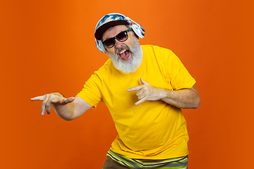 Image showing Senior hipster man using devices, gadgets on orange background. Tech and joyful elderly lifestyle concept