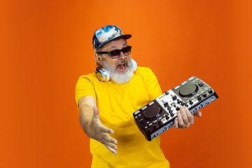 Image showing Senior hipster man using devices, gadgets on orange background. Tech and joyful elderly lifestyle concept