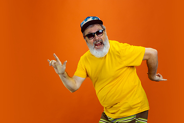 Image showing Senior hipster man using devices, gadgets on orange background. Tech and joyful elderly lifestyle concept