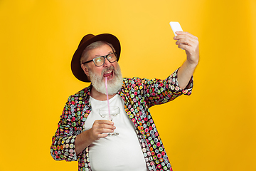 Image showing Senior hipster man wearing eyeglasses posing on yellow background. Tech and joyful elderly lifestyle concept