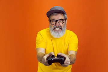 Image showing Senior hipster man using devices, gadgets on orange background. Tech and joyful elderly lifestyle concept