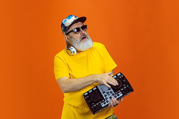 Image showing Senior hipster man using devices, gadgets on orange background. Tech and joyful elderly lifestyle concept