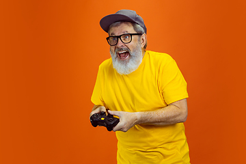 Image showing Senior hipster man using devices, gadgets on orange background. Tech and joyful elderly lifestyle concept