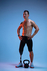 Image showing Athlete with disabilities or amputee isolated on blue studio background. Professional male sportsman with leg prosthesis training with weights in neon