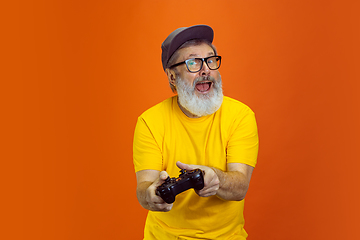 Image showing Senior hipster man using devices, gadgets on orange background. Tech and joyful elderly lifestyle concept