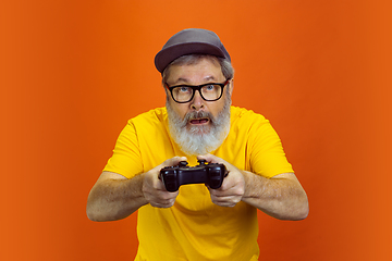 Image showing Senior hipster man using devices, gadgets on orange background. Tech and joyful elderly lifestyle concept