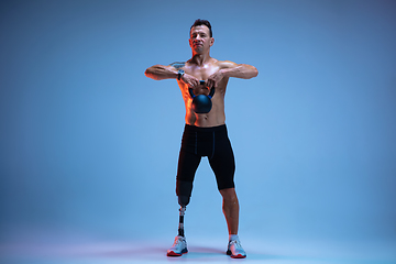 Image showing Athlete with disabilities or amputee isolated on blue studio background. Professional male sportsman with leg prosthesis training with weights in neon