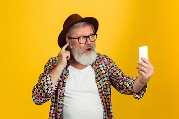 Image showing Senior hipster man wearing eyeglasses posing on yellow background. Tech and joyful elderly lifestyle concept