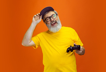 Image showing Senior hipster man using devices, gadgets on orange background. Tech and joyful elderly lifestyle concept