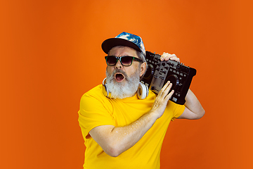 Image showing Senior hipster man using devices, gadgets on orange background. Tech and joyful elderly lifestyle concept