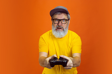 Image showing Senior hipster man using devices, gadgets on orange background. Tech and joyful elderly lifestyle concept