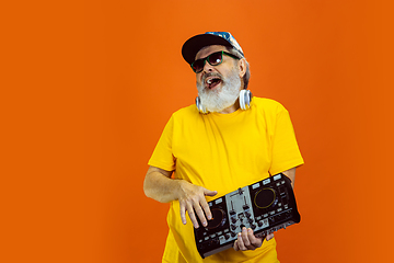 Image showing Senior hipster man using devices, gadgets on orange background. Tech and joyful elderly lifestyle concept