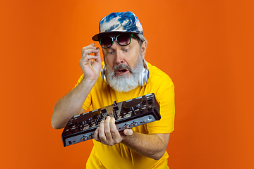 Image showing Senior hipster man using devices, gadgets on orange background. Tech and joyful elderly lifestyle concept