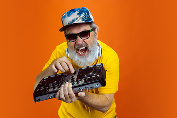 Image showing Senior hipster man using devices, gadgets on orange background. Tech and joyful elderly lifestyle concept