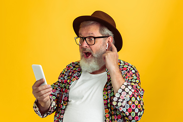 Image showing Senior hipster man wearing eyeglasses posing on yellow background. Tech and joyful elderly lifestyle concept