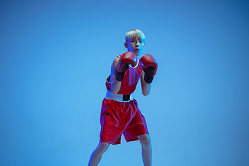 Image showing Teenager in sportswear boxing isolated on blue studio background in neon light