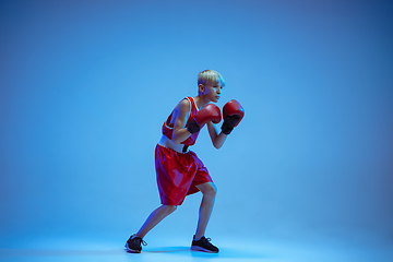 Image showing Teenager in sportswear boxing isolated on blue studio background in neon light