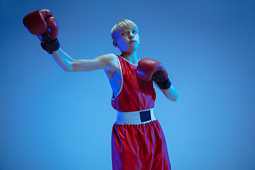 Image showing Teenager in sportswear boxing isolated on blue studio background in neon light