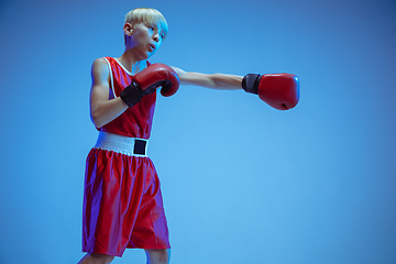 Image showing Teenager in sportswear boxing isolated on blue studio background in neon light