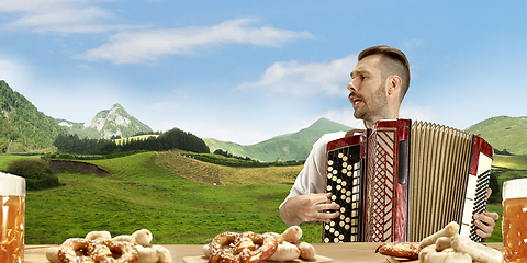 Image showing The happy smiling man with beer dressed in traditional Austrian or Bavarian costume holding mug of beer, mountains on background, flyer