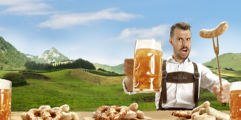 Image showing The happy smiling man with beer dressed in traditional Austrian or Bavarian costume holding mug of beer, mountains on background, flyer