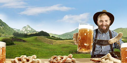 Image showing The happy smiling man with beer dressed in traditional Austrian or Bavarian costume holding mug of beer, mountains on background, flyer